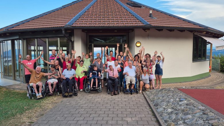 Des personnes se tiennent debout ou en chaise roulante devant un bâtiment, ils sourient