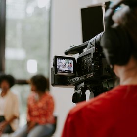 Retombées Journées AVC 2025 Une personne tient une caméra, elle filme deux personnes en arrière-plan