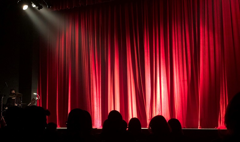 Spectateurs sont de dos et regardent la scène et ses grands rideaux rouges